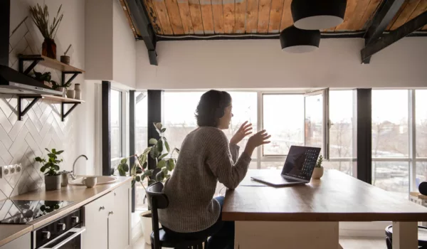 Woman sat in kitchen in a video meeting on her laptop