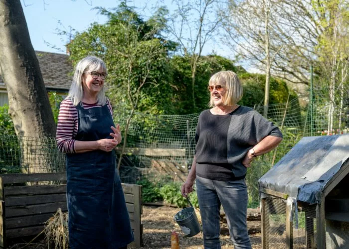 Two women chatting in a garden next to hen hut